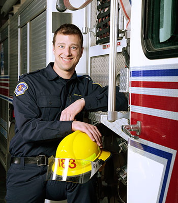 A City of Red Deer Firemedic standing in uniform next to a firetruck