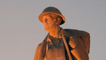 Photograph of the cenotaph of Major Frank Norbury taken at sunset. He is dressed in soldier apparel from the First World War.