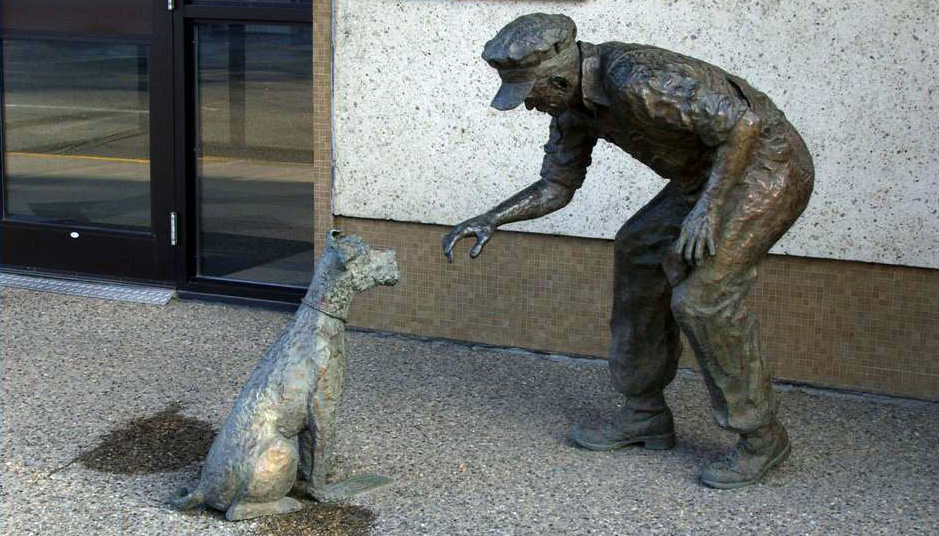 Bronze sculpture of a rail working confronting a little dog who is standing on the man's money.