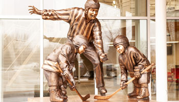 bronze sculpture of two young hockey players and a referee meeting for a face-off