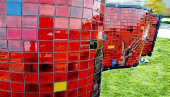 Side view of the red side of a rectangle sculpture made up of glass tiles an the photo etched tiles that show police and emergency services personnel and and out-reading hands trying to join. The word 